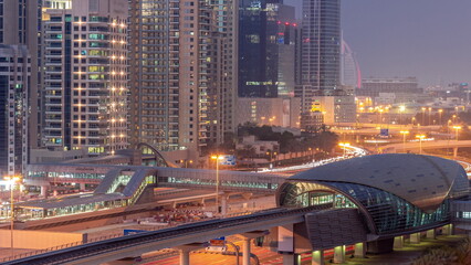 Futuristic building of Dubai metro station and luxury skyscrapers behind in Dubai Marina aerial day to night