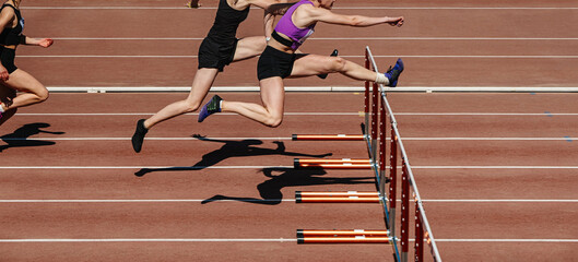 group female athletes run 100 meters with hurdles