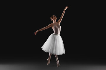 Fototapeta na wymiar Young ballerina practicing dance moves on black background