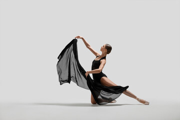 Graceful young ballerina practicing dance moves with black veil on white background