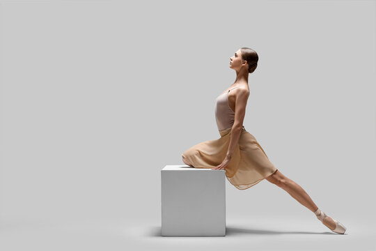 Young ballerina practicing dance moves on cube against white background. Space for text