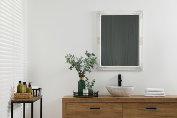 Modern bathroom interior with stylish mirror, eucalyptus branches, vessel sink and wooden vanity