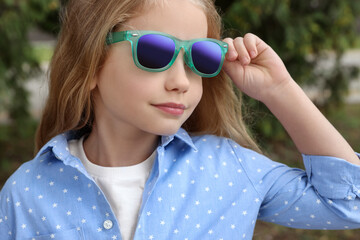 Girl in stylish sunglasses near spruce trees outdoors, closeup