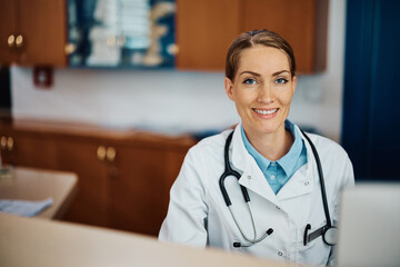 Happy doctor at her desk in office at medical clinic looking at camera.