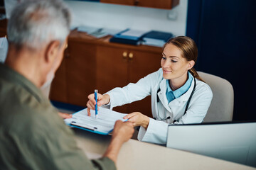 Happy doctor helping her mature patient to fill out medical documents at reception desk.