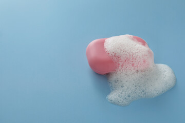 Soap bar with fluffy foam on light blue background, space for text