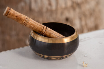 a singing Tibetan bowl stands on a table against the background of a palm tree trunk in the...