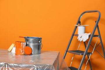 Can with paint, brush and renovation equipment on table against orange background