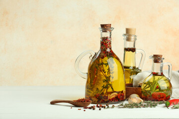Cooking oil with different spices and herbs in jugs on white wooden table. Space for text