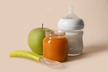 Healthy baby food in jar, bottle of milk, apple and spoon on beige background