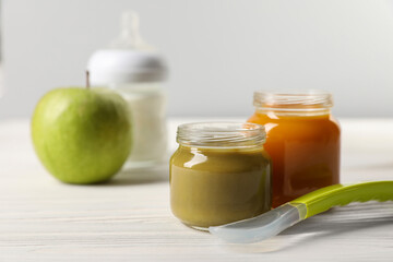 Jars with healthy baby food and spoon on white wooden table. Space for text