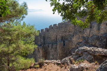 Fototapeta na wymiar Fragment of a stone wall with battlements of the old fortress of the city of Alanya, Turkey. Mediterranean Sea in the background
