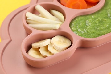 Healthy baby food. Section plate with delicious broccoli puree, vegetables and fruit on yellow background, closeup