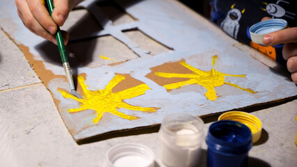 6 year old child is painting sun, window and house on paper. Brush in hand. Drawing with colored gouache paints on cardboard. Creative and Artistic hobby. Happy future concept. Kid dream. Handicraft