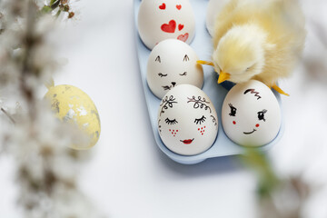 Defocused focus on foreground. Beautiful hand-painted Easter eggs in a blue tray. Yellow little chicken on eggs on white background. Minimal concept. Easter card with copy space. Soft Selective focus