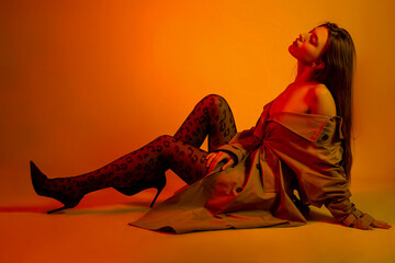 Beautiful young brown hair girl sitting sexy on a floor in leopard tights and in cloak in colored...