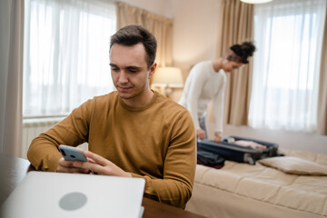 couple family life caucasian man working on laptop computer or making online reservations while his wife young woman is packing or unpack baggage suitcase on bed in hotel room real people copy space