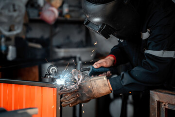 Male welding is connecting steel work in a small factory. Welding steel, wheel, wearing gloves, masks, preventing smoke and sparks from welding