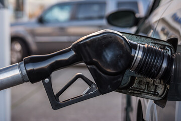 gasoline pump nosel in car gas tank at gas station with suv in background