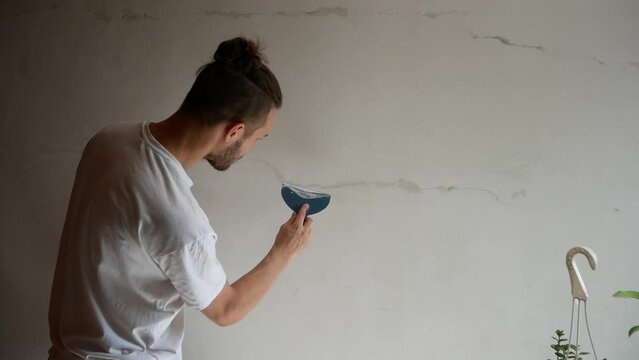 Young White Man Applies Putty on a White Wall to Fill Cracks