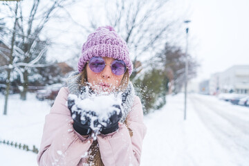A woman with sunglasses on blowing snow off her palms to the camera. High quality photo
