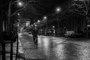 A man speeds by on a bicycle in blur over a cobblestone road with the Arc de Triomphe in the...