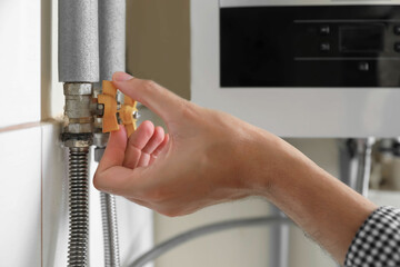 Man turning on valve of gas boiler, closeup