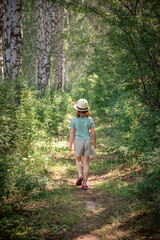 Naklejka na ściany i meble a cute girl in a straw hat walks along a path in the woods in the summer