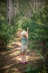 a cute girl in a straw hat walks along a path in the woods in the summer