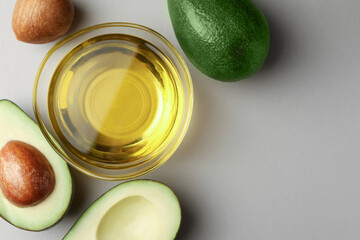 Cooking oil in bowl and fresh avocados on light grey background, flat lay. Space for text