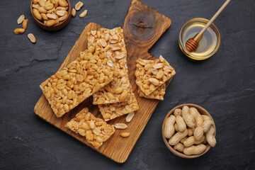 Delicious peanut bars (kozinaki) and ingredients on black table, flat lay
