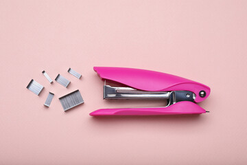 New bright stapler with staples on pink background, fat lay. School stationery