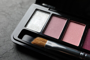 Beautiful eye shadow palette with brush on dark grey textured table, closeup