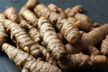 Many raw turmeric roots on black textured table, closeup