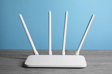 New white Wi-Fi router on wooden table against light blue background