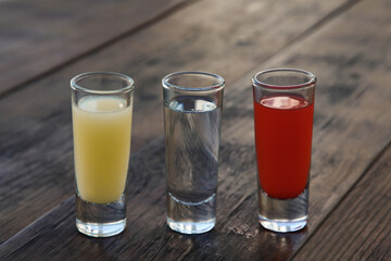 Shots with lime juice, tequila and sangria as colors of mexican flag on wooden table. Traditional serving