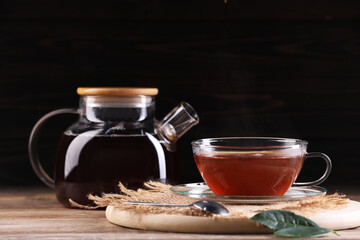 Aromatic hot tea in glass cup and teapot on wooden table. Space for text