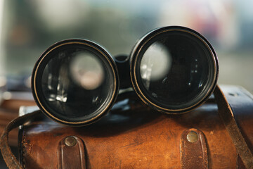 Vintage military binoculars, laying on the brown leather case. Blurry background.