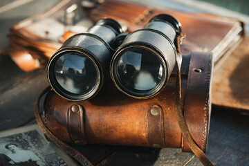 Vintage military binoculars, laying on the brown leather case on the wooden brown table.