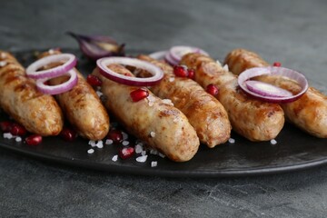 Tasty grilled sausages with onion rings and pomegranate seeds served on grey table, closeup