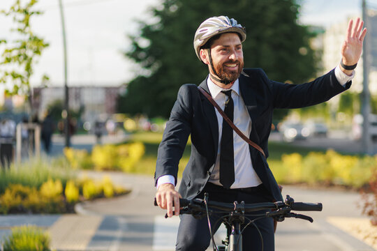 Happy office clerk waving hand, greeting, while riding bike outdoor.