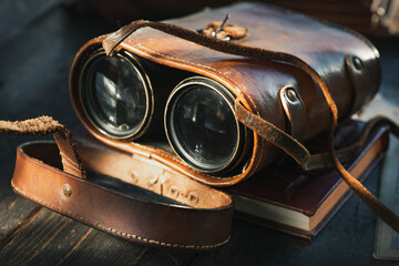 Vintage military binoculars in the leather case, laying on the wooden brown table.