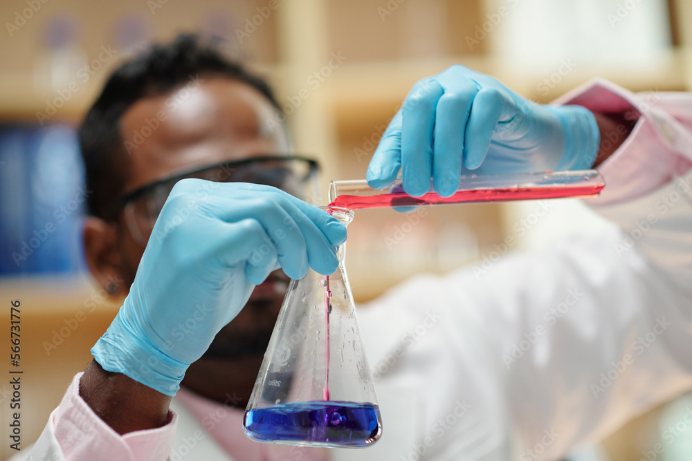 Wall mural close-up image of scientist pouring red reagent in flask with bue liquid