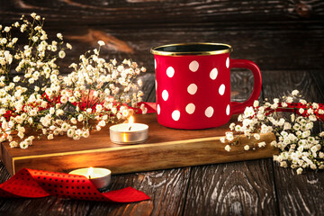 Obraz na płótnie Canvas Red cup with white polka dots, candles, gypsophila flowers and red ribbon. Romantic composition on a dark wooden background. Concept for Valentine's Day