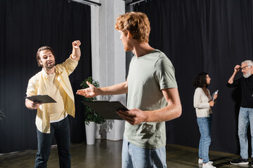 redhead and bearded actors holding clipboards with screenplays while rehearsing in theater.