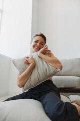 Teenage girl smile everyone sits at home near the couch and tosses up pillows, fun game and happiness without filters, copy place