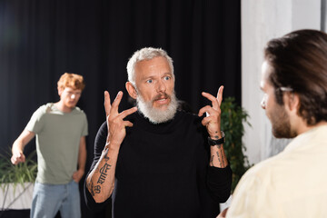 bearded art director gesturing while talking to blurred actor in theater