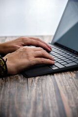 Close-up of a woman's hands working with a laptop on a wooden table.