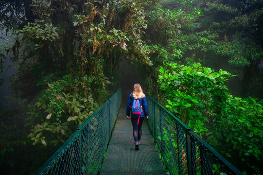 Young girl walking across bridge in lush jungle with tall trees in Costa Rica