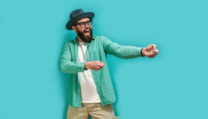 Purposeful man in a hat with a beard, pulling an invisible rope, demonstrates his perseverance and leadership qualities, striving to achieve the goal. Isolated on a blue studio background.